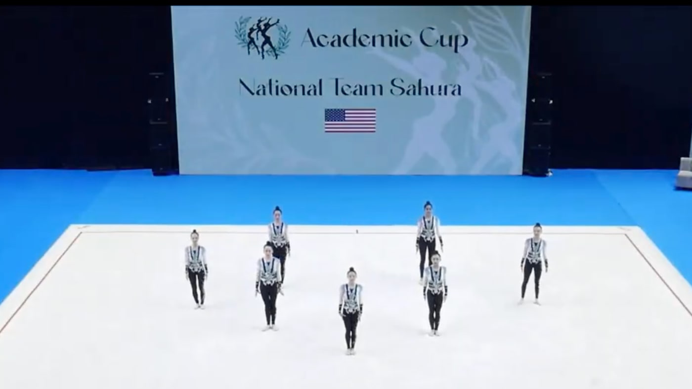 Seven AGG gymnasts standing in formation on a competition floor.