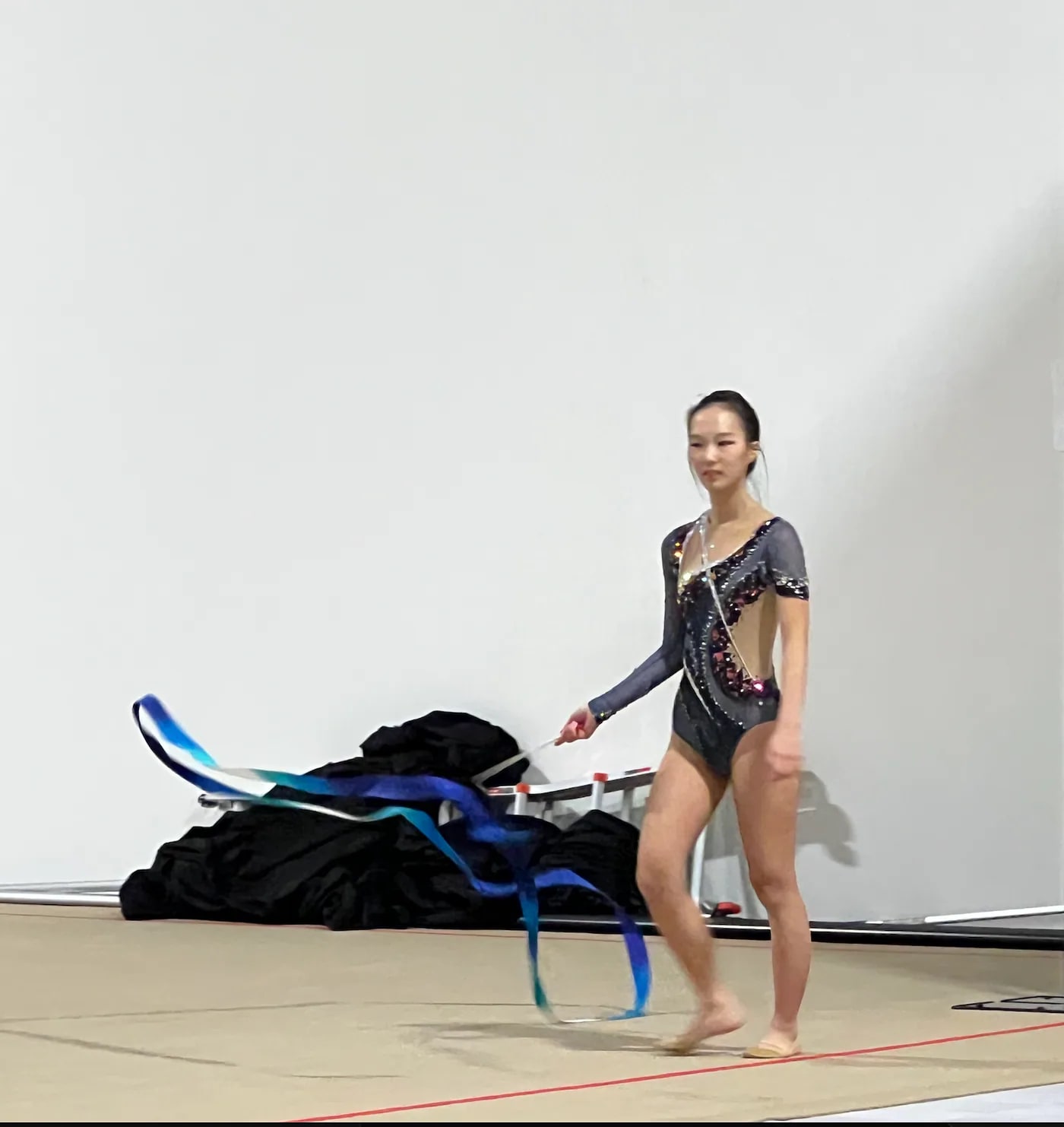 Lynn holding a blue ribbon on a rhythmic-gymnastics floor.